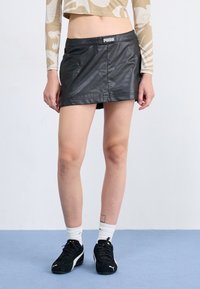Black faux leather mini skirt with a smooth texture, featuring a branded waistband. Paired with black sneakers and white crew socks.