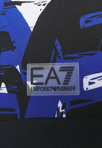 Modrá a černá sportovní tkanina s dynamickým abstraktním vzorem; zahrnuje průhlednou nášivku loga EA7 Emporio Armani.