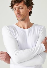 Witte langwerpige shirt met lange mouwen van zachte katoen. Beschikt over een ronde halslijn en aangesloten mouwen. Getextureerde stof met een gladde afwerking.