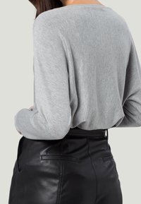 Haut long en tricot doux gris, présentant une coupe décontractée et un col large, associé à un pantalon en cuir noir taille haute avec poches arrière.