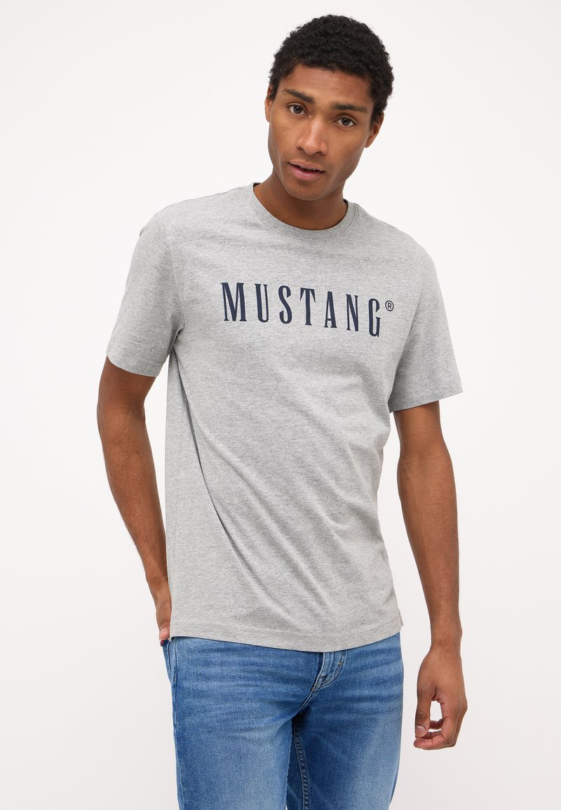 Halliset halli puuvillane T-särk, millel on laia laeva "MUSTANG" logo rinnal, ümmargune kaelus ja lühikesed varrukad. Mugav lõige ja sile tekstuur.