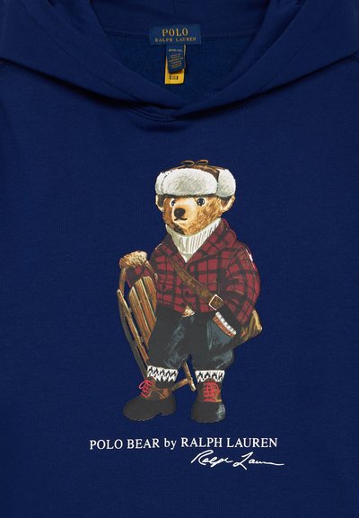 Námornícky mikina s grafikou medveďa v zimnom oblečení, vrátane károvaného saka, pleteného šálu a sánok. Text "POLO BEAR by RALPH LAUREN" pod ním.