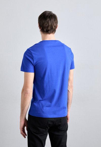 Camiseta de algodón azul de manga corta con cuello redondo, corte relajado y textura suave, combinada con pantalones negros.