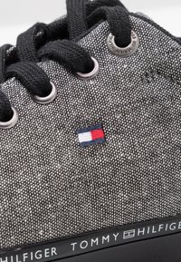 Sneaker testurizzato nero e grigio con lacci neri, occhielli in metallo e logo ricamato rosso, bianco e blu. Presenta una suola nera con marchio.