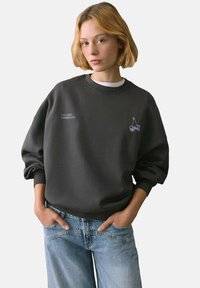 Dunkelgrauer Sweatshirt aus weichem Material, mit rundem Ausschnitt, oversized Schnitt, gesticktem Kirschdesign und gerippten Bündchen.