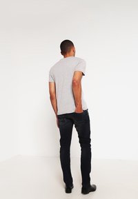 Grå kortärmad t-shirt med rund halsringning, ihopparad med mörkblå jeans och svarta skor, sedd bakifrån.