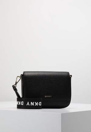 Schwarze Leder-DKNY-Umhängetasche mit magnetischer Klappe und abnehmbarem Markenstoffriemen, liegend auf weißem Sockel.