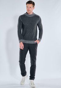 Gray knitted sweater with a high neck and ribbed hem. Features contrasting striped shoulder details. Paired with dark trousers and white sneakers.