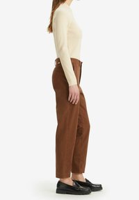 Beżowa, prążkowana bluzka z długim rękawem, zestawiona z brązowymi spodniami o wysokim stanie i czarnymi półbutami. Prosty design, dopasowany krój i gładka faktura.
