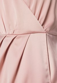 Tissu rose doux avec des plis et des fronces subtils, comportant des coutures croisées créant un design structuré et superposé.