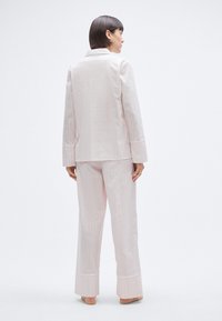 Ensemble de pyjama rose clair avec des rayures verticales. Le haut à manches longues a un col, et le pantalon a de larges revers aux chevilles.