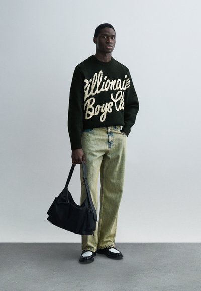 Μαύρο πλεκτό πουλόβερ με την επιγραφή «Billionaire Boys Club» σε κρεμ χρώμα, σε συνδυασμό με ανοιχτό πράσινο ριγέ παντελόνι και μαύρη τσάντα ώμου. Λευκά και μαύρα παπούτσια.