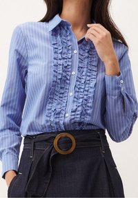 Blusa a righe blu con fronte arricciato, dettagli con bottoni e maniche lunghe, abbinata a una gonna in denim scuro a vita alta con una fibbia circolare.