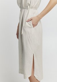 Gai bēšs midi kleitas ar sānu kabatām, jostu viduklī un šķēlumu kreisajā pusē. Izgatavota no teksturēta, viegla auduma.