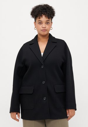 Black oversized blazer with notched collar, three front buttons, and two patch pockets. Made of a smooth fabric with a soft texture.