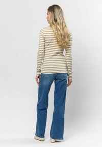 Svītrains gariem piedurknēm krekls bēšā un krēmkrāsā, apvienots ar ziliem platiem džinsiem. Kreklam ir pieguļošs dizains un ribota tekstūra.