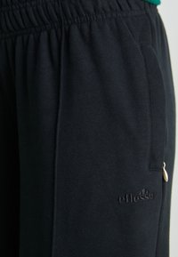 Svarta sweatpants i mjukt tyg, med elastisk midja, sidficka och tonad logobroderi nära fållen.