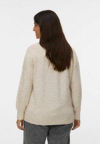 Pull crème avec un motif texturé de points en relief, manches longues et poignets côtelés. Associe à un pantalon gris.