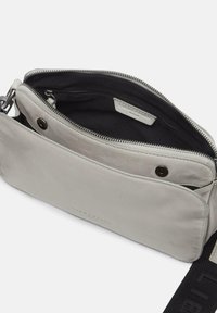 Grau Ledertasche mit glatter Textur, Reißverschluss und einer Innentasche mit Reißverschluss. Verfügt über einen schwarzen Trageriemen mit eingeprägtem Logo.