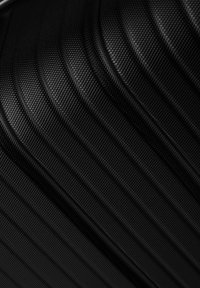 Valigia nera con texture a righe verticali, realizzata in materiale resistente, con una superficie liscia e sottili motivi per migliorare la presa.