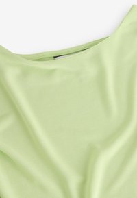 Tejido de jersey de color verde claro y suave con una textura lisa. Presenta un escote amplio y se drapea suavemente, creando un ajuste relajado.