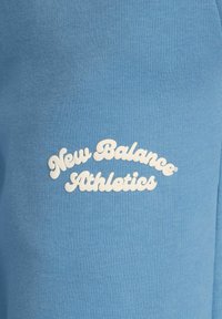 Light blue fabric t-shirt featuring raised white text, "New Balance Athletics," in a curved design, showcasing a smooth texture.