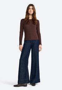 Maglietta a maniche lunghe ribbed marrone abbinata a jeans larghi in denim scuro. I jeans presentano un orlo piegato e un sottile dettaglio di cucitura. Scarpe flat marroni.
