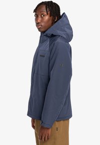 Marineblaue isolierte Jacke mit strukturierter Oberfläche, verstellbarem Kapuze, aufgesetztem Reißverschluss und elastischen Bündchen. Mit sichtbarem Logo auf der Brust.
