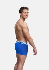 Blå bomullsboxer med ett vitt elastiskt midjeband med "MOKKO" tryckt. Designen är figurnära och slät, vilket betonar formen och texturen.