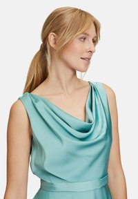 Ein türkisfarbenes Satin-Kleid mit drapiertem Cowl-Ausschnitt und nahtlosen Schultern. Es hat eine figurbetonte Taille und eine glatte Textur.