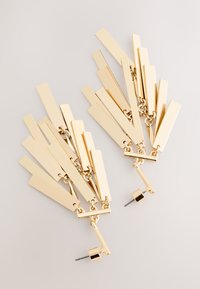 Örhängen i guldton med ljuskronaformat, bestående av förlängda rektangulära former sammanlänkade med kedjor, med en stiftlåsning för säker användning.