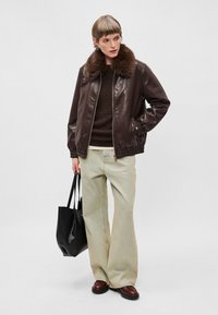 Brun læder bomberjakke med pelskrave, lyse brede jeans og en sort tote taske, båret med brune læderstøvler.