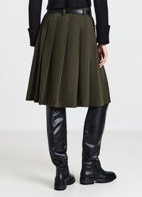 Gonna plissettata verde oliva con una texture liscia, fascia in vita nera, abbinata a stivali neri lucidi al ginocchio.