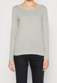 Lichtgrijze longsleeve t-shirt van een zachte, rekbare stof met een ronde hals en afgeronde onderkant, gecombineerd met donkere jeans.
