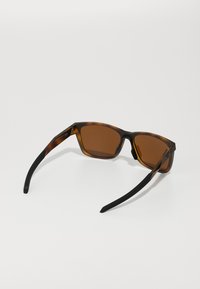 Gafas de sol de tono marrón con una montura de carey, acentos negros, forma rectangular y brazos negros estilizados.