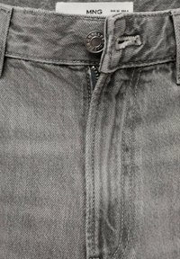 Jean en denim gris avec une braguette zippée et une fermeture par bouton métallique, doté d'une ceinture standard et d'une texture subtile. Le tissu présente un léger motif de tissage.