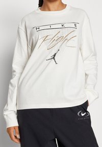 Weißes langärmliges T-Shirt mit Grafikdruck, der "NIKE" und eine Silhouette eines Basketballspielers zeigt. Weicher Stoff, lockere Passform.