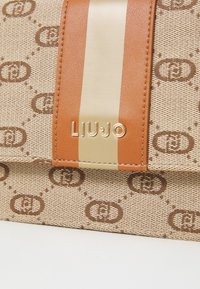 Beige handbag featuring interlocking logo pattern, tan and cream stripes, gold hardware accent, and textured fabric. Brand label: LIU JO.