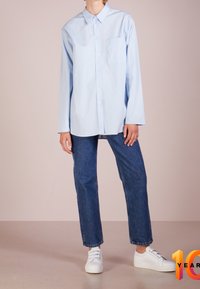 Light blue button-up shirt with a collar and a chest pocket, worn with dark blue straight-leg jeans and white sneakers.