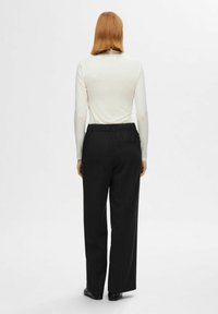Weißes langärmeliges Oberteil und schwarze weit geschnittene Hose mit elastischem Bund, von hinten betrachtet. Glatte Texturen, einfaches Design, keine Muster.