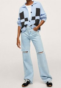 Cárdigan de canalé azul claro con acentos negros estampados, combinado con jeans de pierna ancha de lavado claro con detalles desgastados y zapatillas negras.