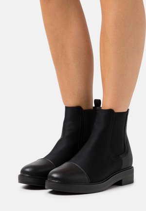 Bottines noires à cheville avec un embout en cuir lisse et des panneaux latéraux élastiques. Présentent un bout arrondi et un petit talon empilé.
