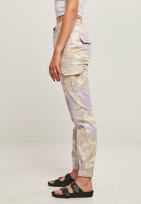 Beige camo cargo bukser med lilla accenter, med sidelommer, elastiske manchetter og en afslappet pasform. Båret med sorte sandaler.