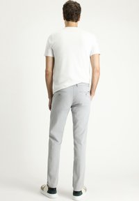 Pantalones gris ajustados con dos bolsillos traseros, combinados con una camiseta blanca lisa y zapatillas blancas. Textura de tela suave y diseño a medida.