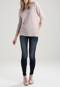 Hellrosa gestrickter Pullover mit Dreiviertelärmeln, kombiniert mit dunklen Skinny Jeans und blassrosa Schuhen. Das Outfit hat einen lässigen Look.