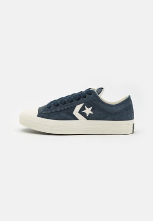 Zapatillas bajas de ante en color azul marino con suela de goma blanca, punta redonda y sistema de cordones. Presentan un logo de estrella en el lado exterior.