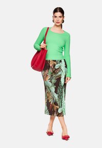 Grüner strukturiertes Langarmoberteil, brauer Rock mit Blumenmuster und grünen Karoelementen sowie roter Handtasche. Rote Schuhe mit Schleifen vervollständigen das Outfit.