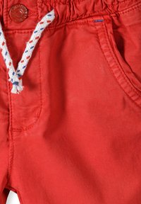 Röda bomullsshorts med elastiskt midjeband, dekorativ snörning i vitt, blått och rött, med en sidoficka.