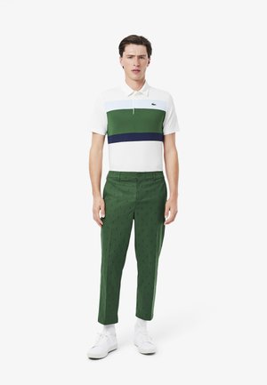 Polo shirt in wit, groen en marineblauw gestreept; slim-fit groene broek met een patroon; gedragen met witte sneakers.