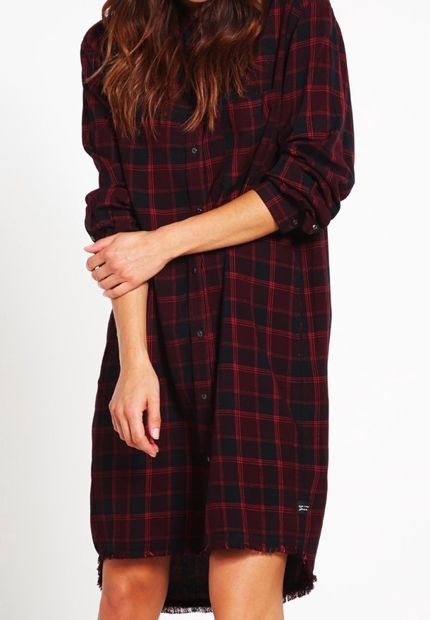 Robe chemise à carreaux rouge et noir en tissu avec des manches longues, fermeture à boutons, ourlet effiloché et coupe ample.
